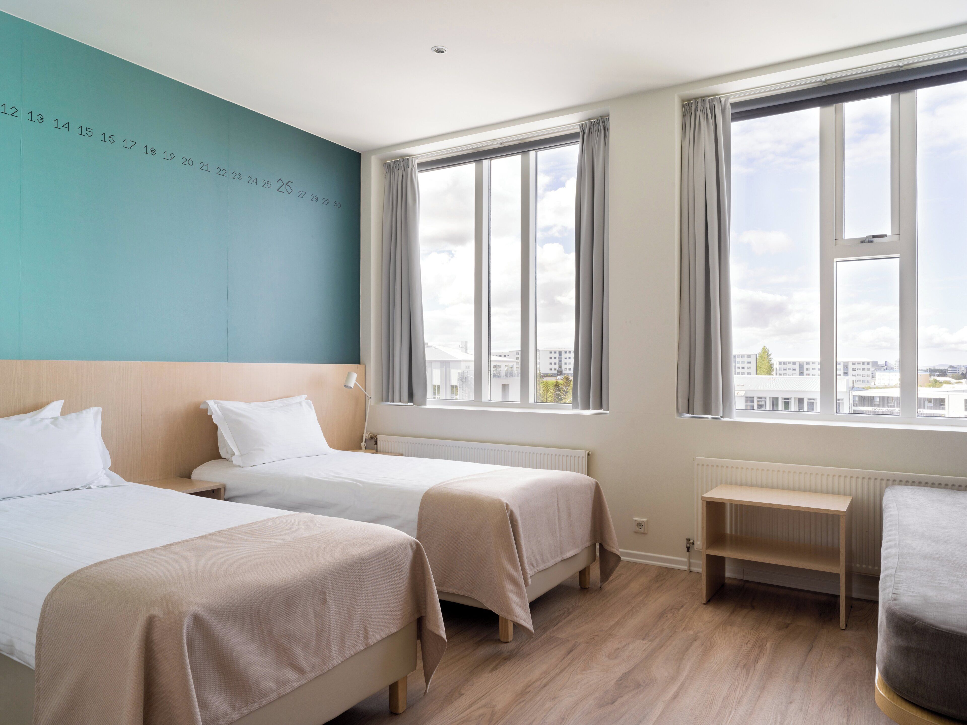 Une chambre d’hôtel avec deux lits, une vue sur les immeubles à travers de grandes fenêtres et un mur orné de chiffres.