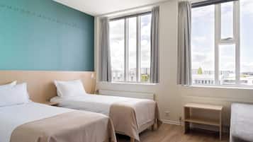 Une chambre d’hôtel avec deux lits, une vue sur les immeubles à travers de grandes fenêtres et un mur orné de chiffres.