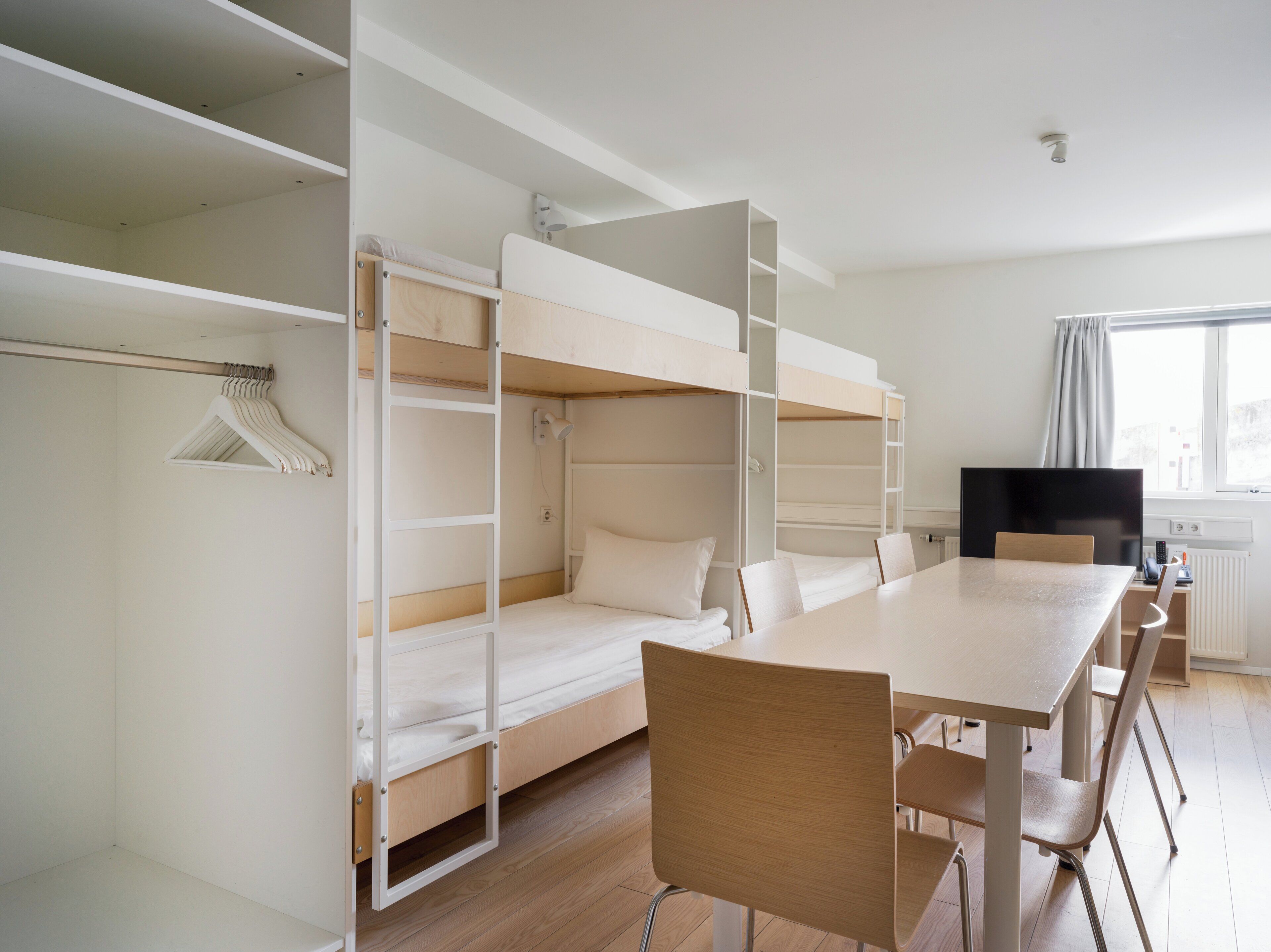 Une pièce avec des lits superposés, une table, des chaises, un téléviseur et une fenêtre avec des rideaux.