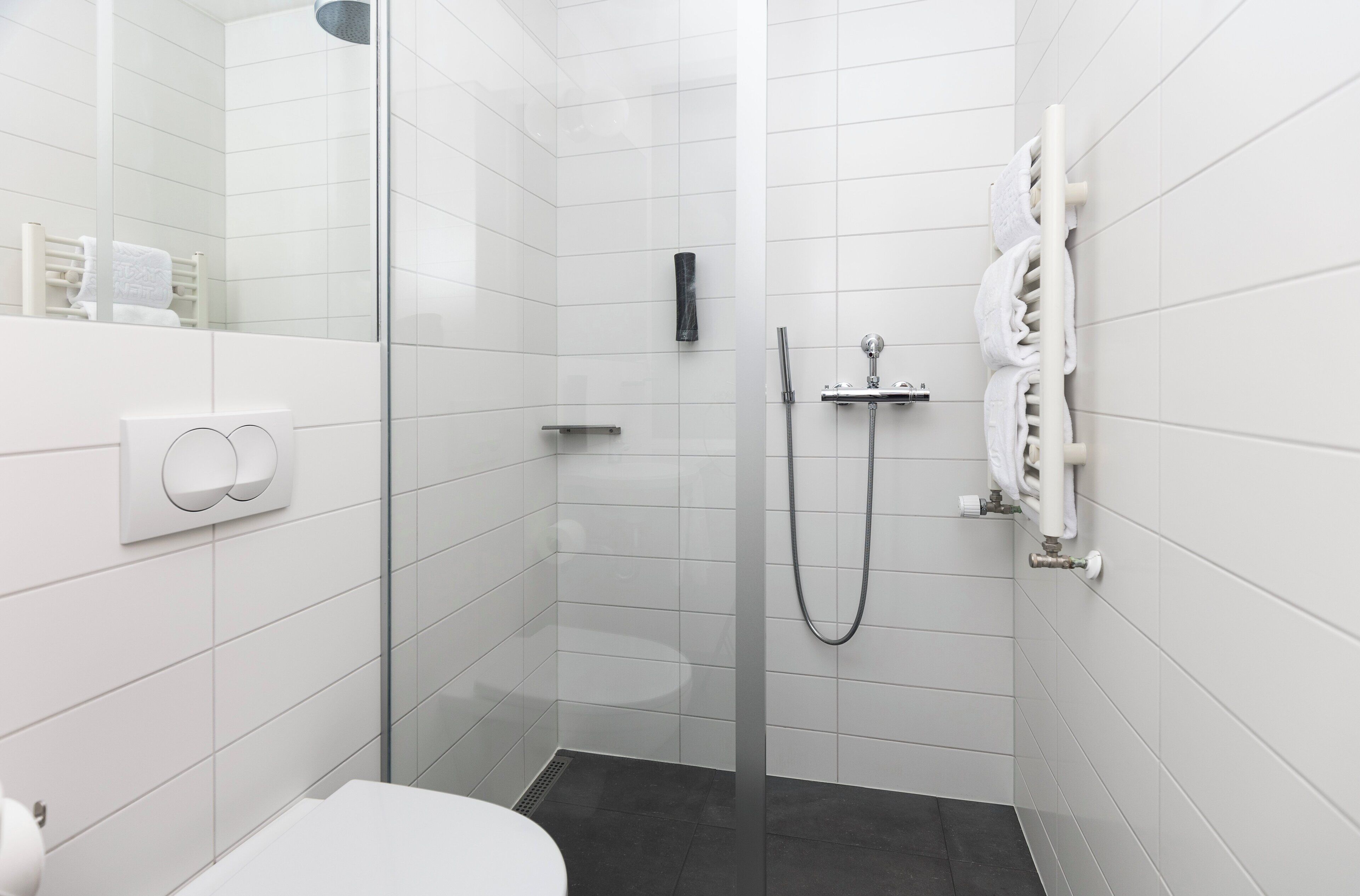 Un baño moderno con paredes de azulejos blancos, cerramiento de ducha de cristal, inodoro y perchero.