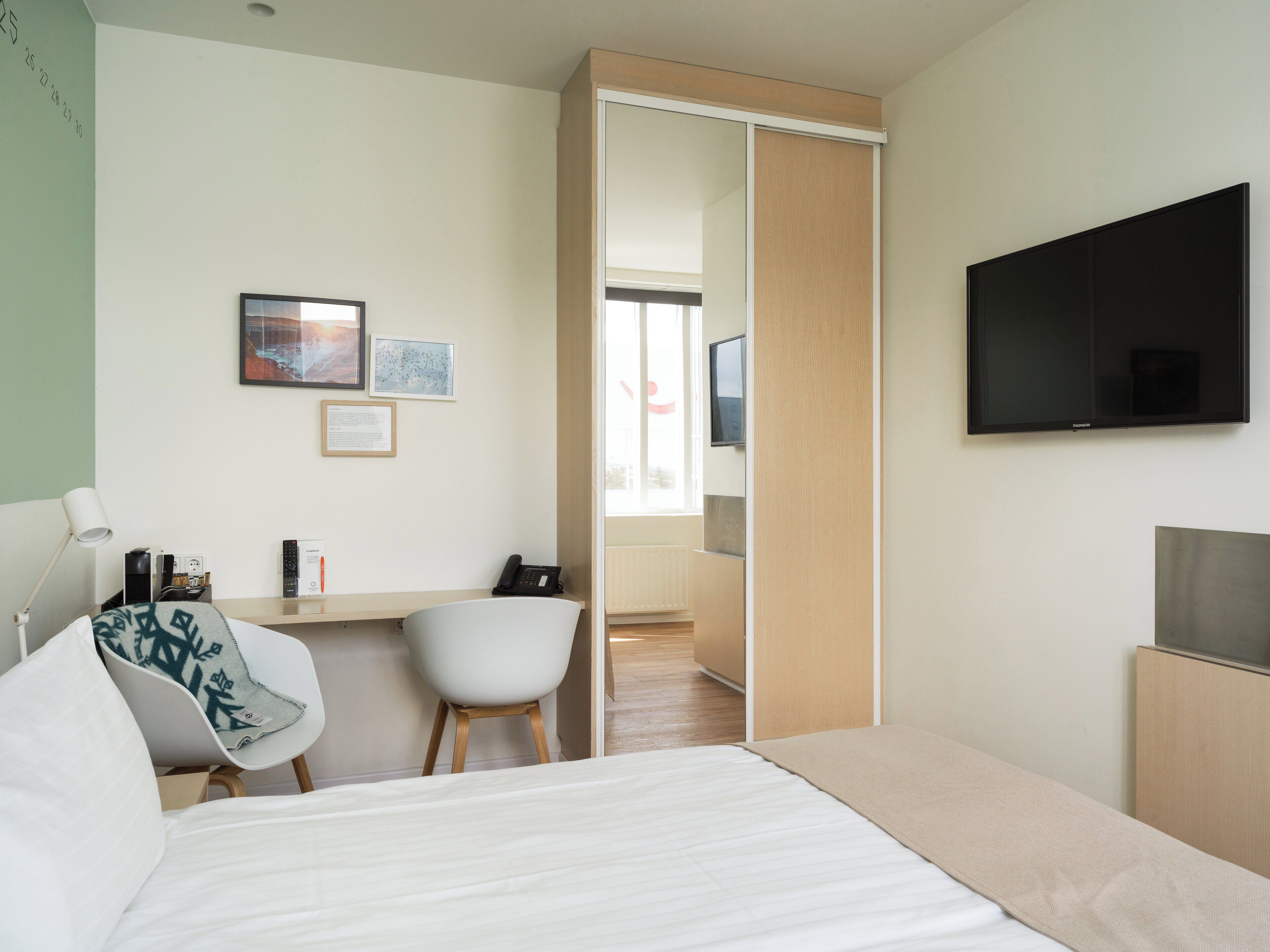 Habitación de hotel moderna con cama, escritorio con silla, televisor de pantalla plana y puerta corredera que da al baño.