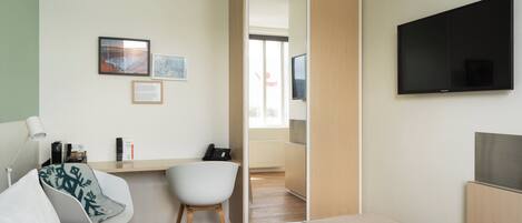 Habitación de hotel moderna con cama, escritorio con silla, televisor de pantalla plana y puerta corredera que da al baño.