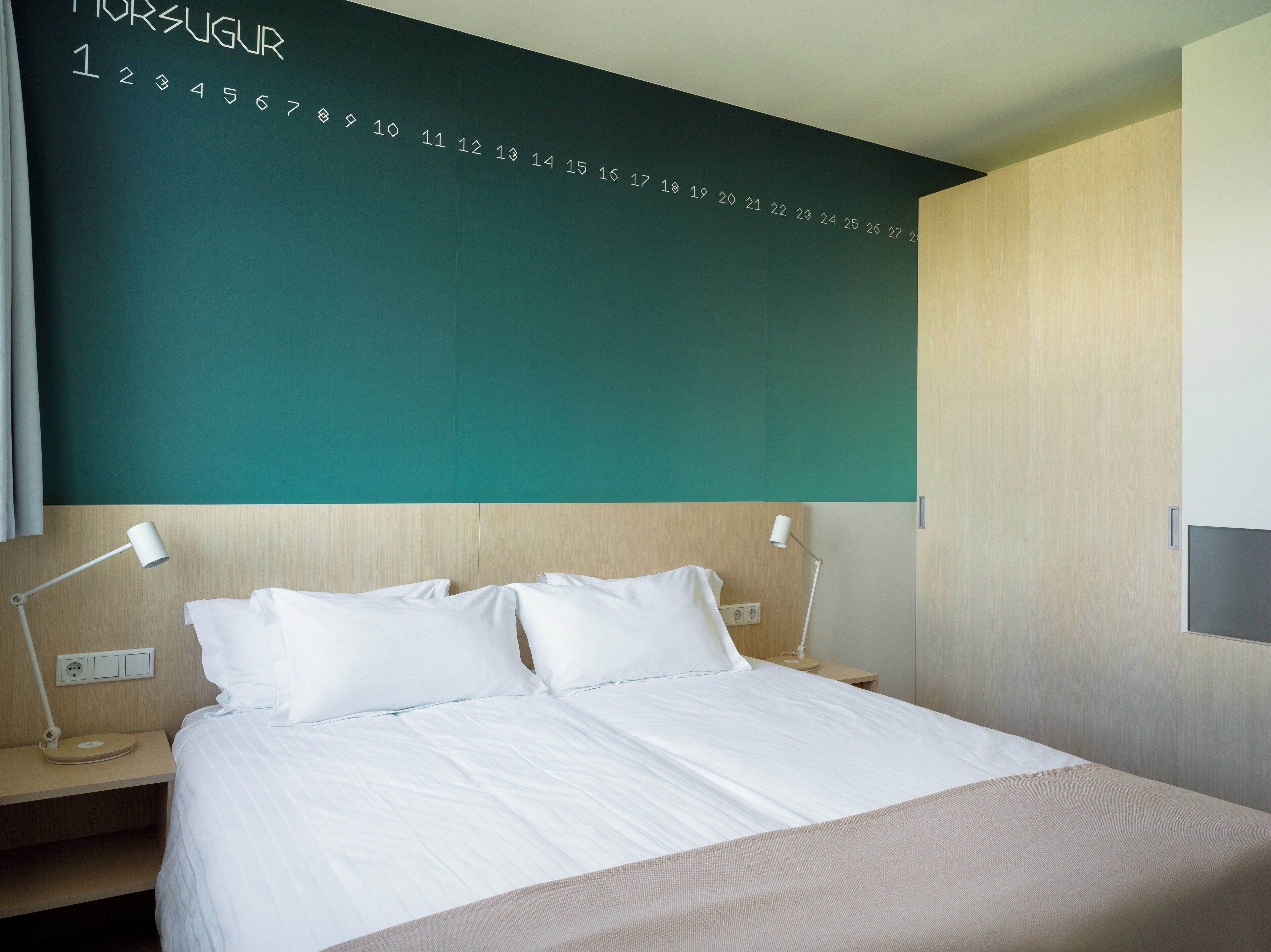A modern hotel room with a large bed, two bedside tables with lamps, and a wall with numbers.