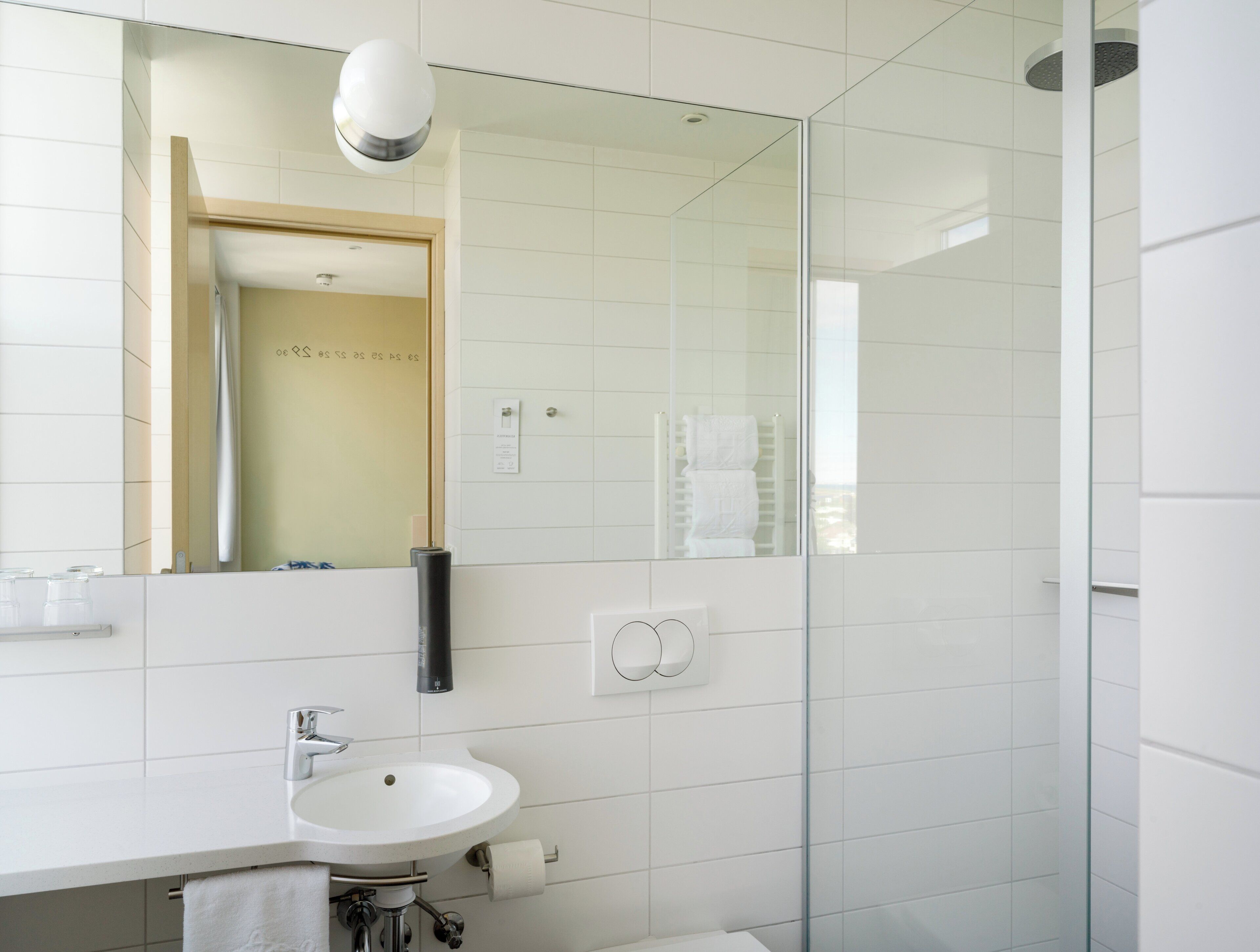 A modern bathroom with a white sink, mirror, and glass shower enclosure.