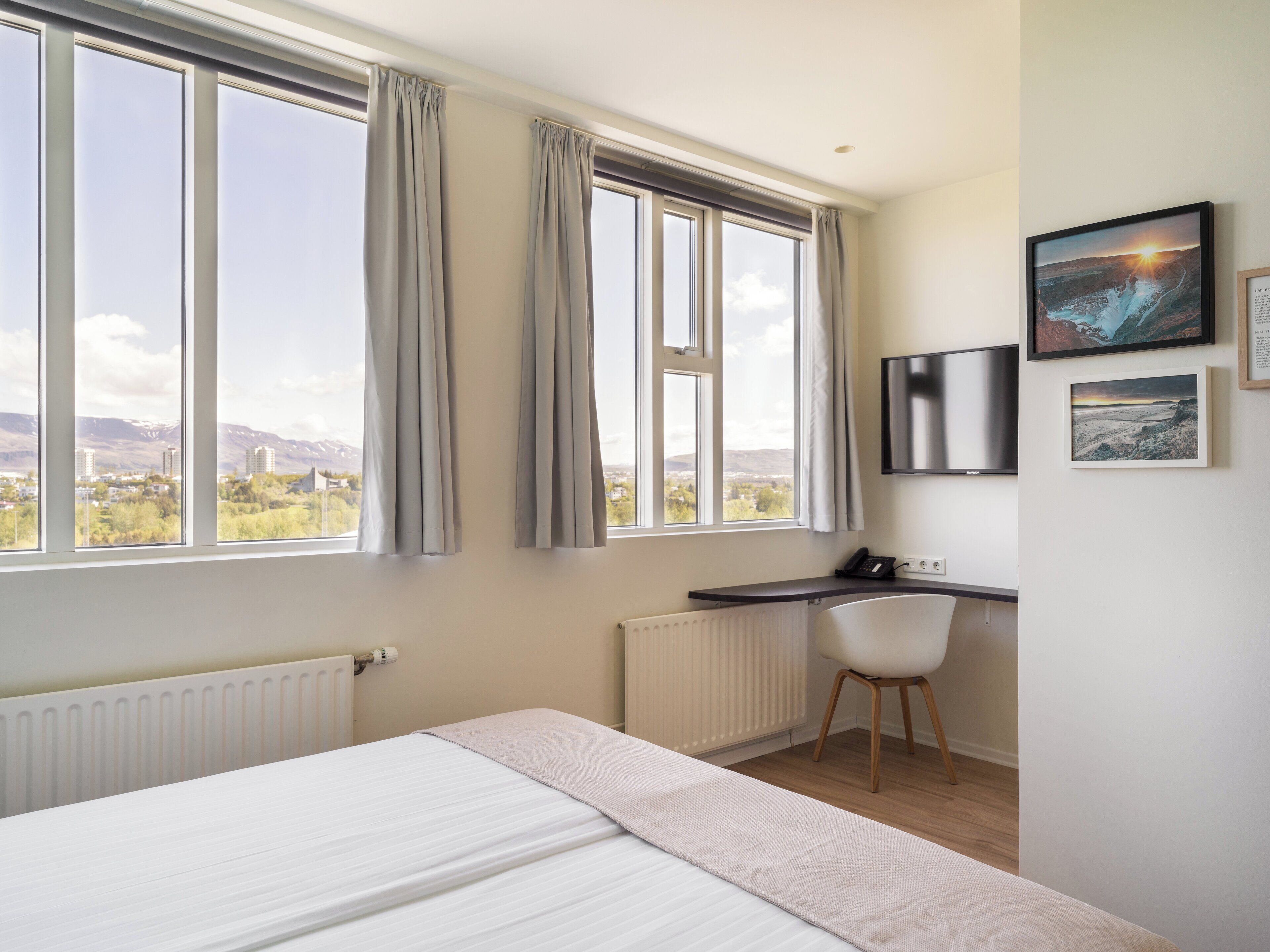 A bedroom with a bed, a desk, a chair, and a view of a mountainous landscape through large windows.