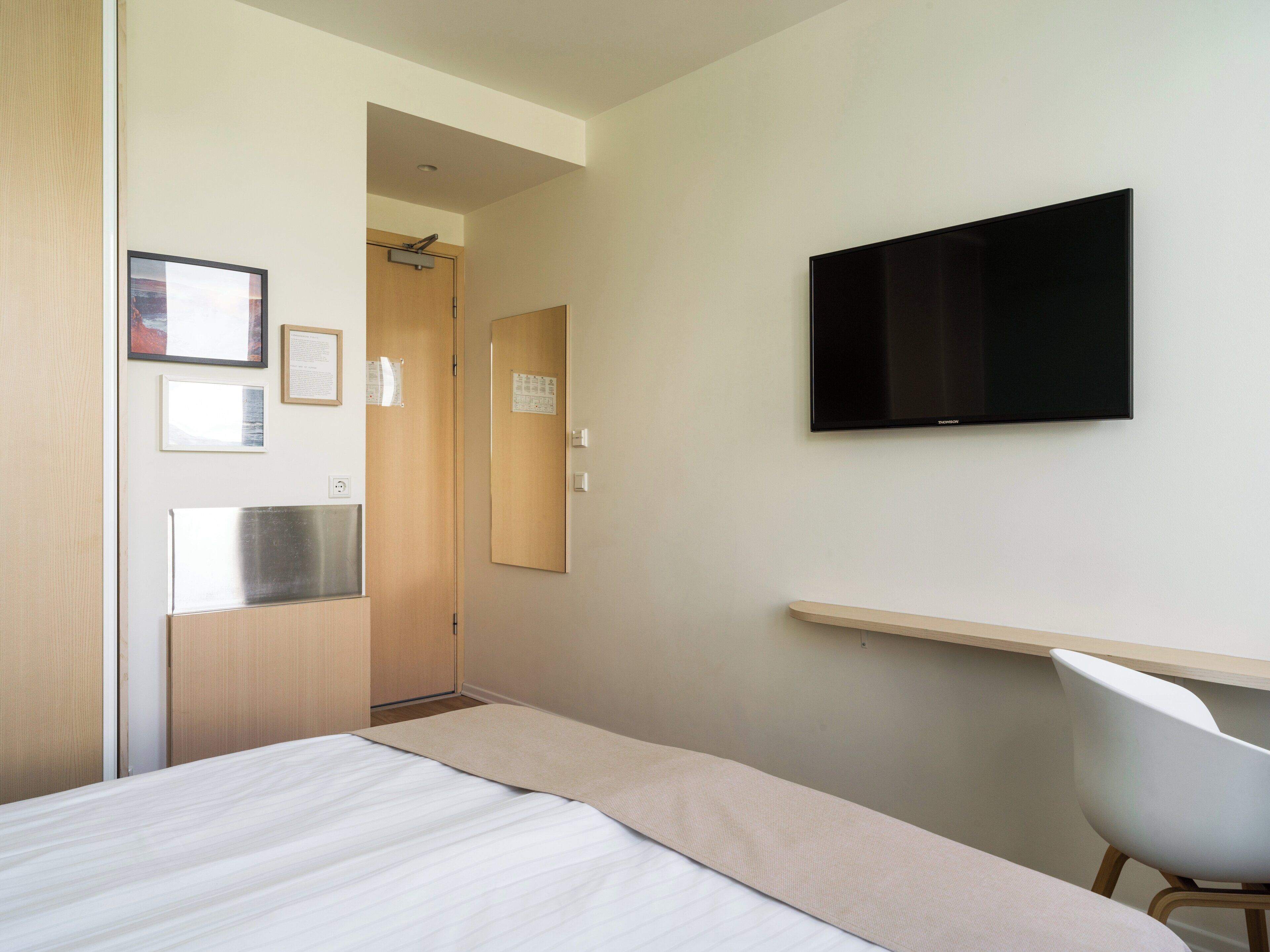 Une chambre d’hôtel avec un lit, un bureau, une chaise, une télévision et une porte.