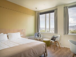 Una habitación de hotel con cama, una silla, una mesita y ventana con vista a la ciudad.