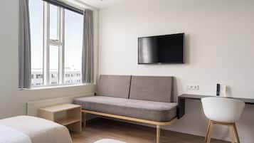 Una habitación de hotel moderna con un ventanal grande, una televisión de pantalla plana, un sofá, un escritorio y una silla.