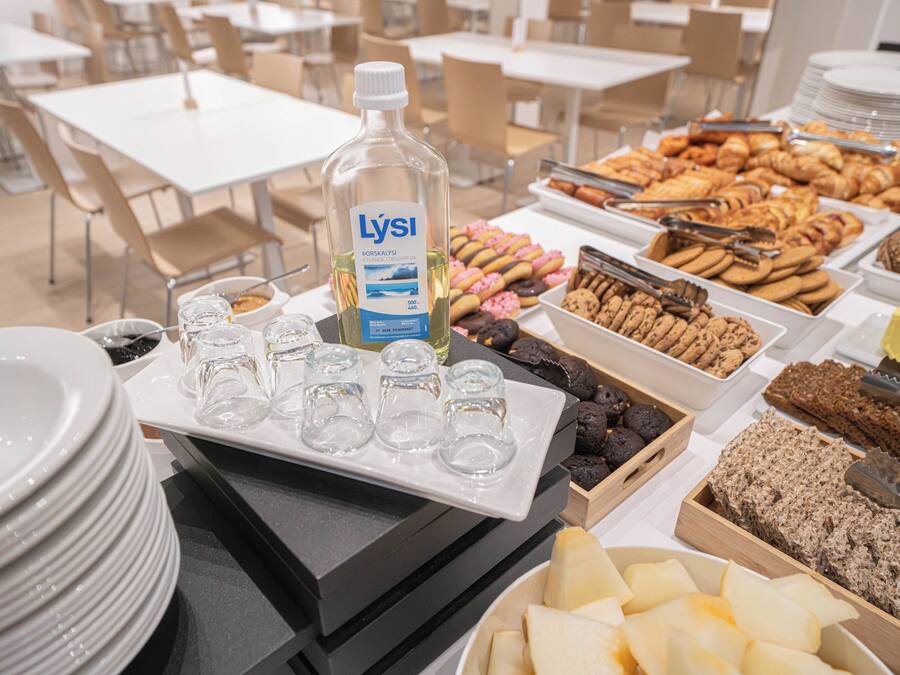 Mesa de buffet com diversos alimentos, incluindo doces, biscoitos e uma garrafa de óleo Lysi.