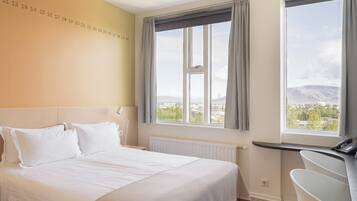 A hotel room with a bed, a desk, a view of a cityscape, and a wall with numbers.