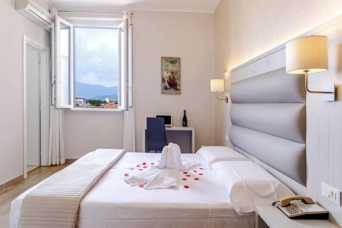 A hotel room with a bed, a desk, a chair, a lamp, and a telephone.