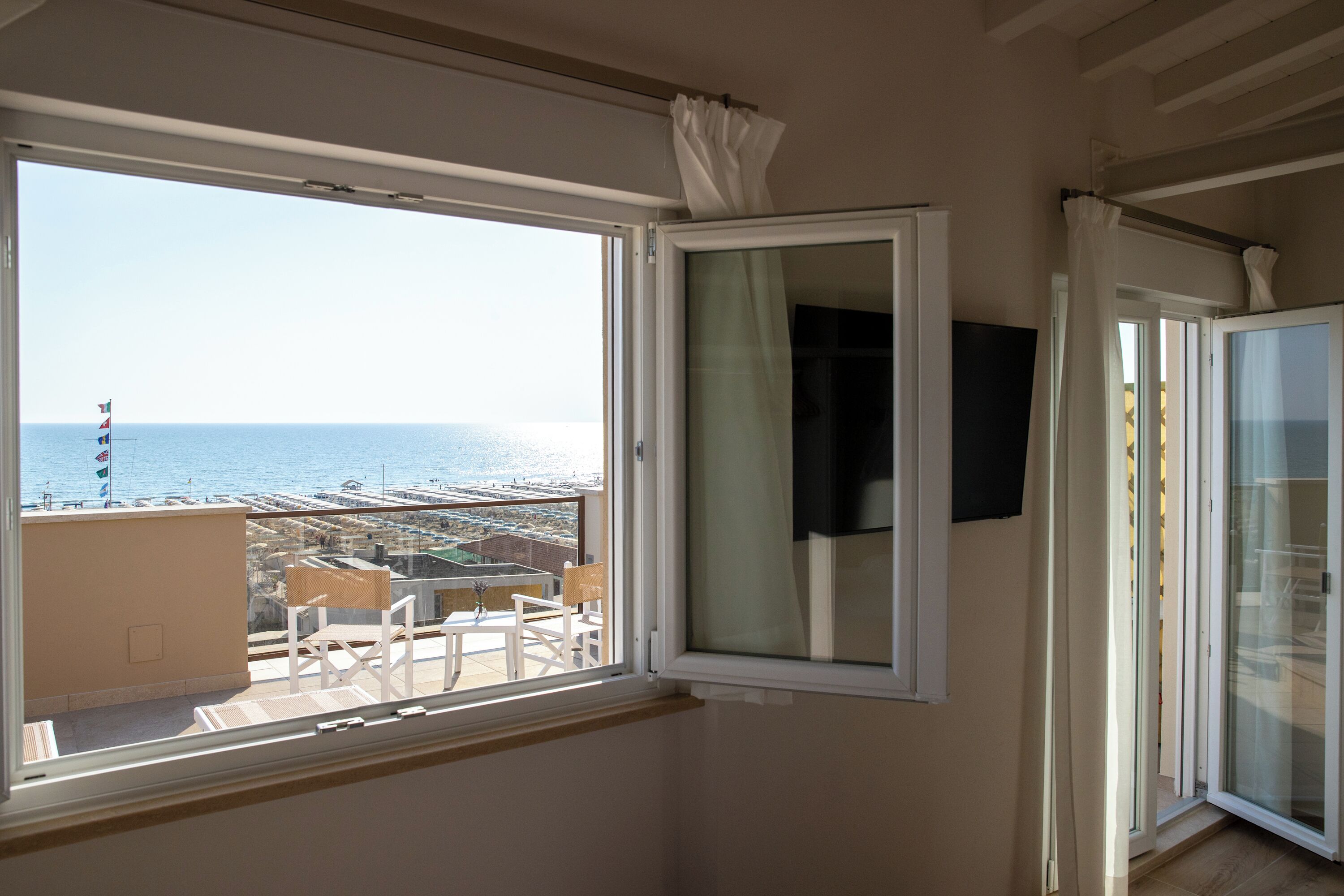 A room with a large window offering a view of the sea and buildings.