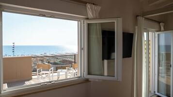 A room with a large window offering a view of the sea and buildings.