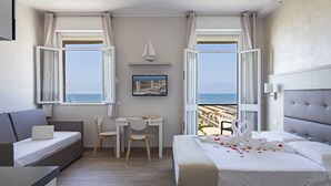 Habitación de hotel con cama, escritorio, una silla y dos ventanas que dan a la playa.