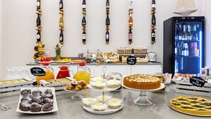 A breakfast buffet with various pastries, a fruit display, and a refrigerator stocked with beverages. - Hotel Biagi (Camaiore)