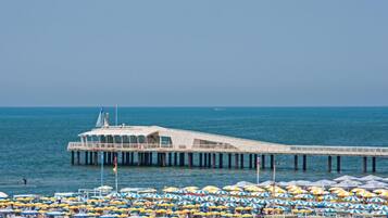 Un muelle que se adentra en el mar con un edificio en la parte superior, rodeado de numerosos sombrillas de playa.
