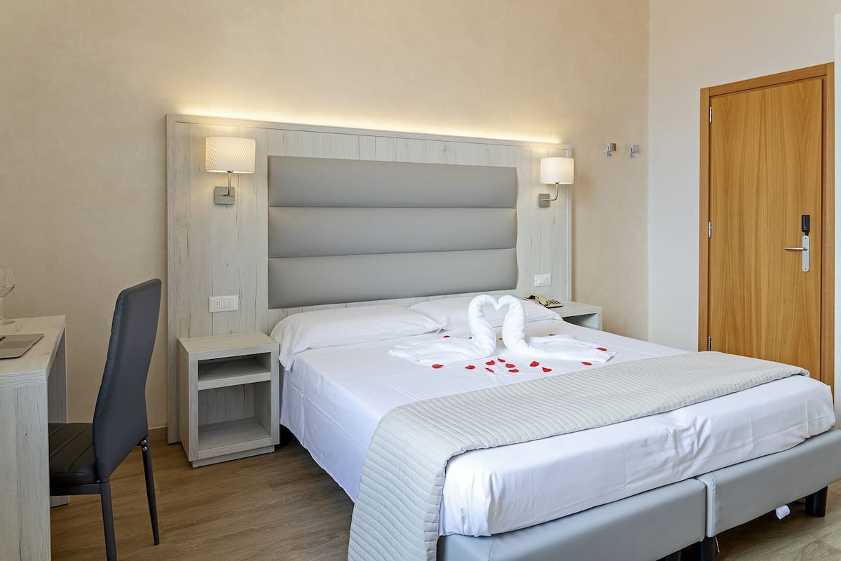 A hotel room with a large bed, a desk, and a chair.