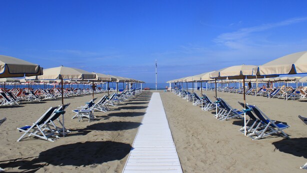A beach with rows of sun loungers and umbrellas, a white walkway, and a clear blue sky. - Hotel Biagi (Camaiore)