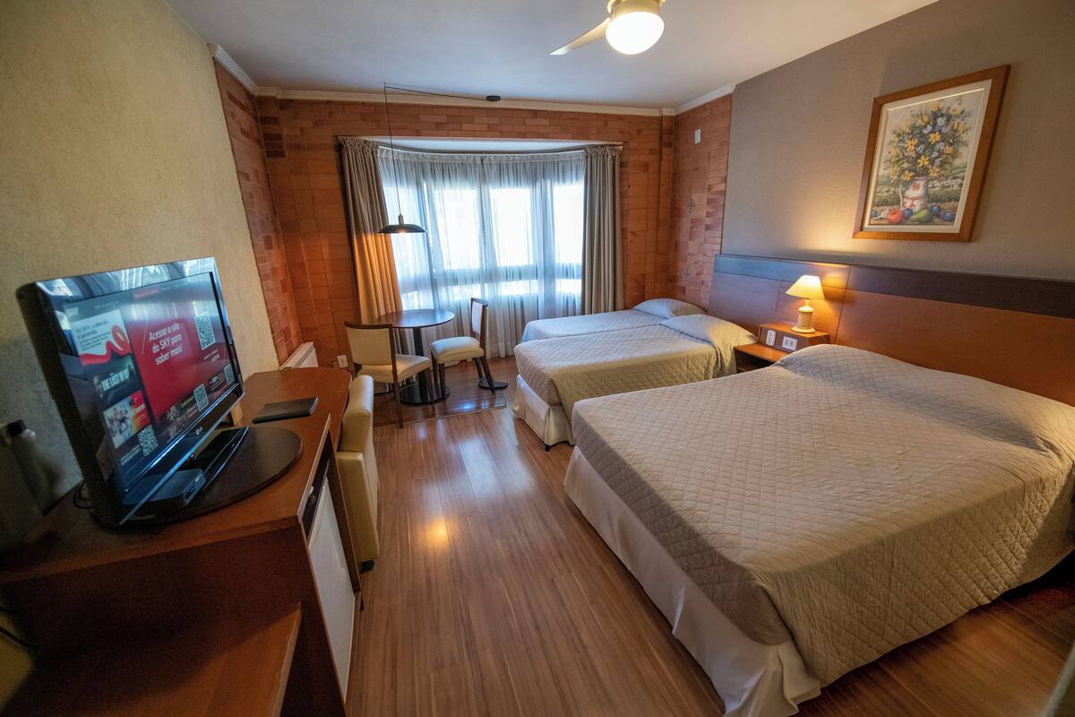 Habitación de hotel con dos camas, televisión, escritorio, silla y ventana con cortinas.