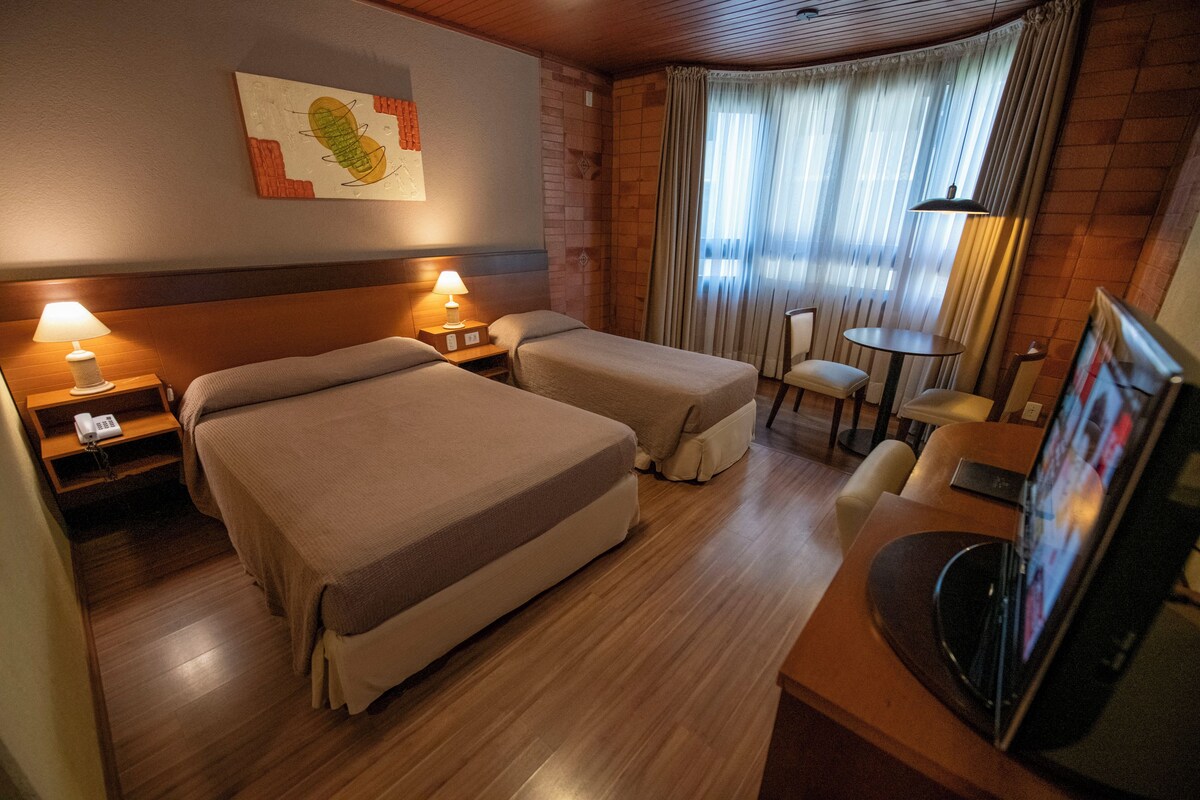 A hotel room with two beds, a desk, a chair, a TV, and a window with curtains.