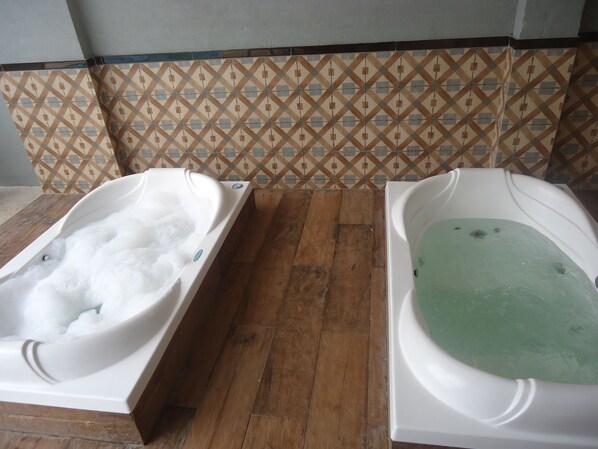 Two hot tubs with water, one with bubbles and the other with a greenish hue, on a wooden floor with patterned tiles in the background.