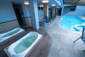 A pool area with two hot tubs, a staircase, and a seating area with chairs and a potted plant.