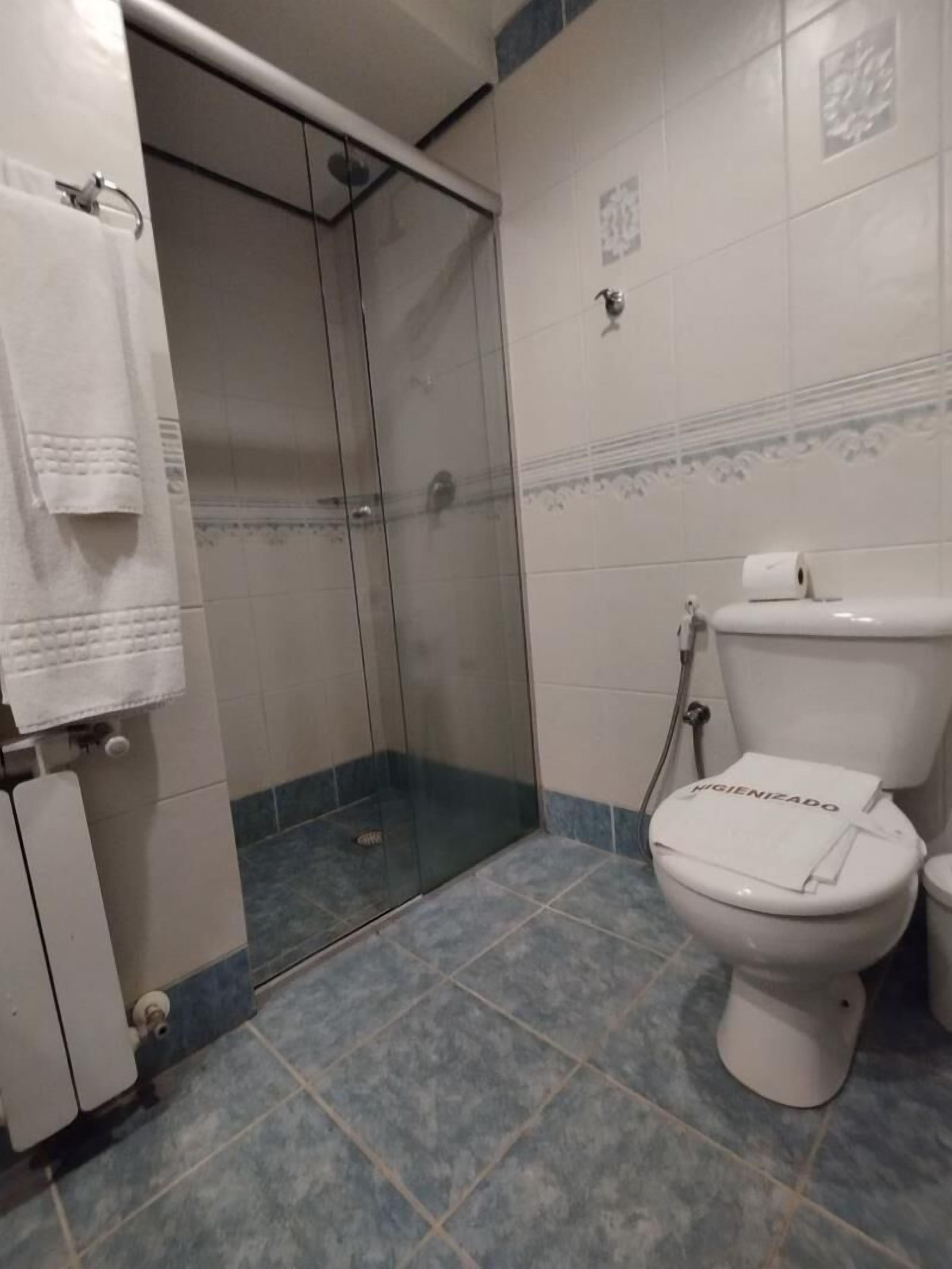 A bathroom with a glass-enclosed shower, a toilet with a paper towel dispenser, and a towel rack.
