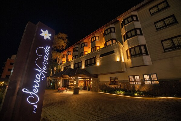 A hotel entrance with a sign, paved walkway, and illuminated windows. - Hotel Serra Nevada (Canela)