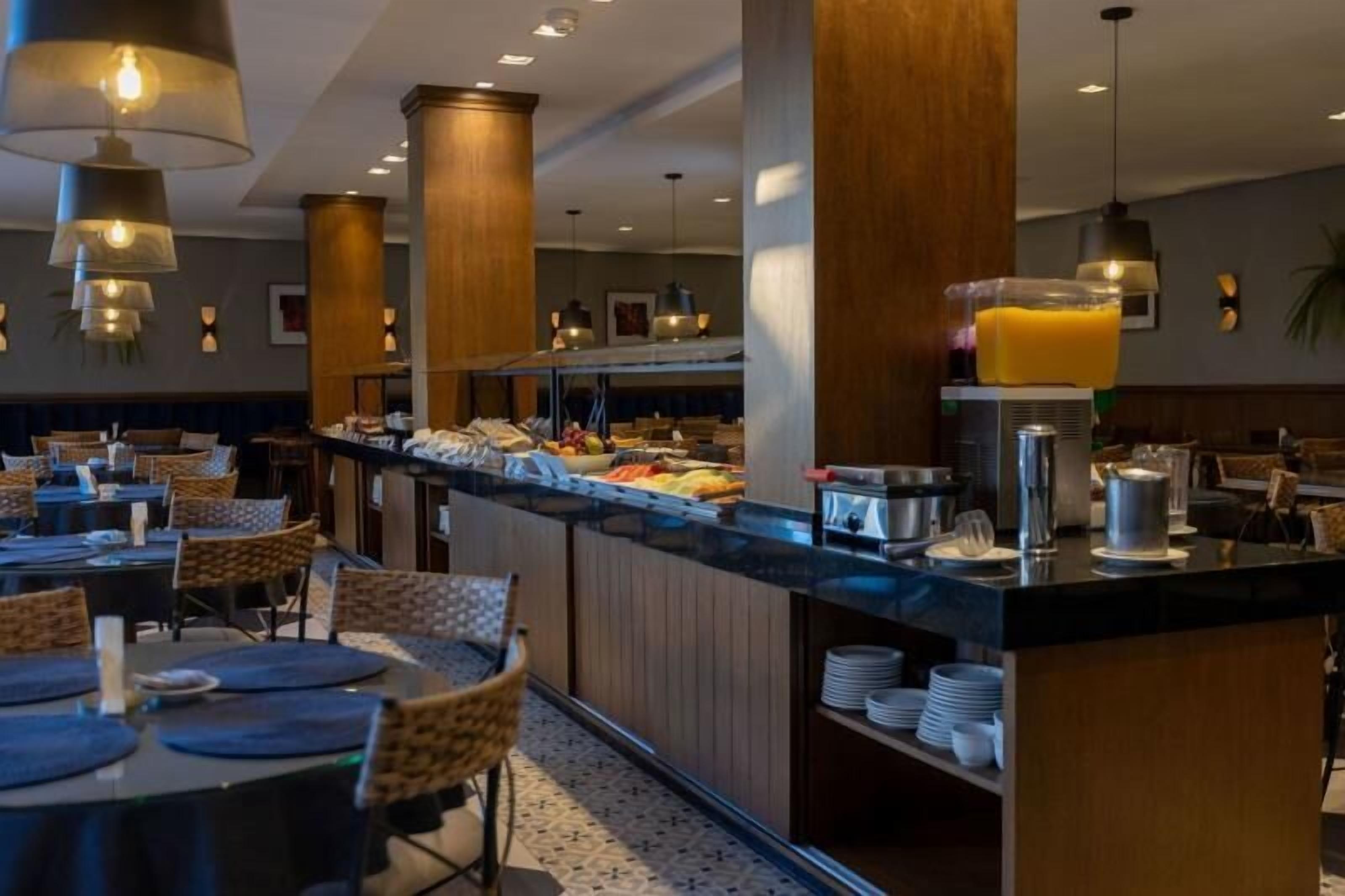 A hotel breakfast area with a buffet counter, dining tables, and chairs.