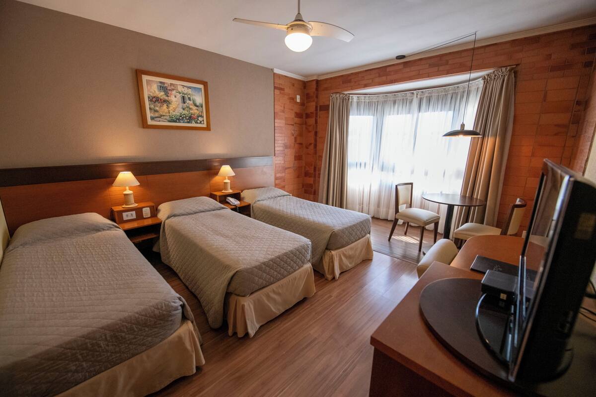 Habitación de hotel con dos camas, un escritorio, una silla, un televisor y una ventana con cortinas.