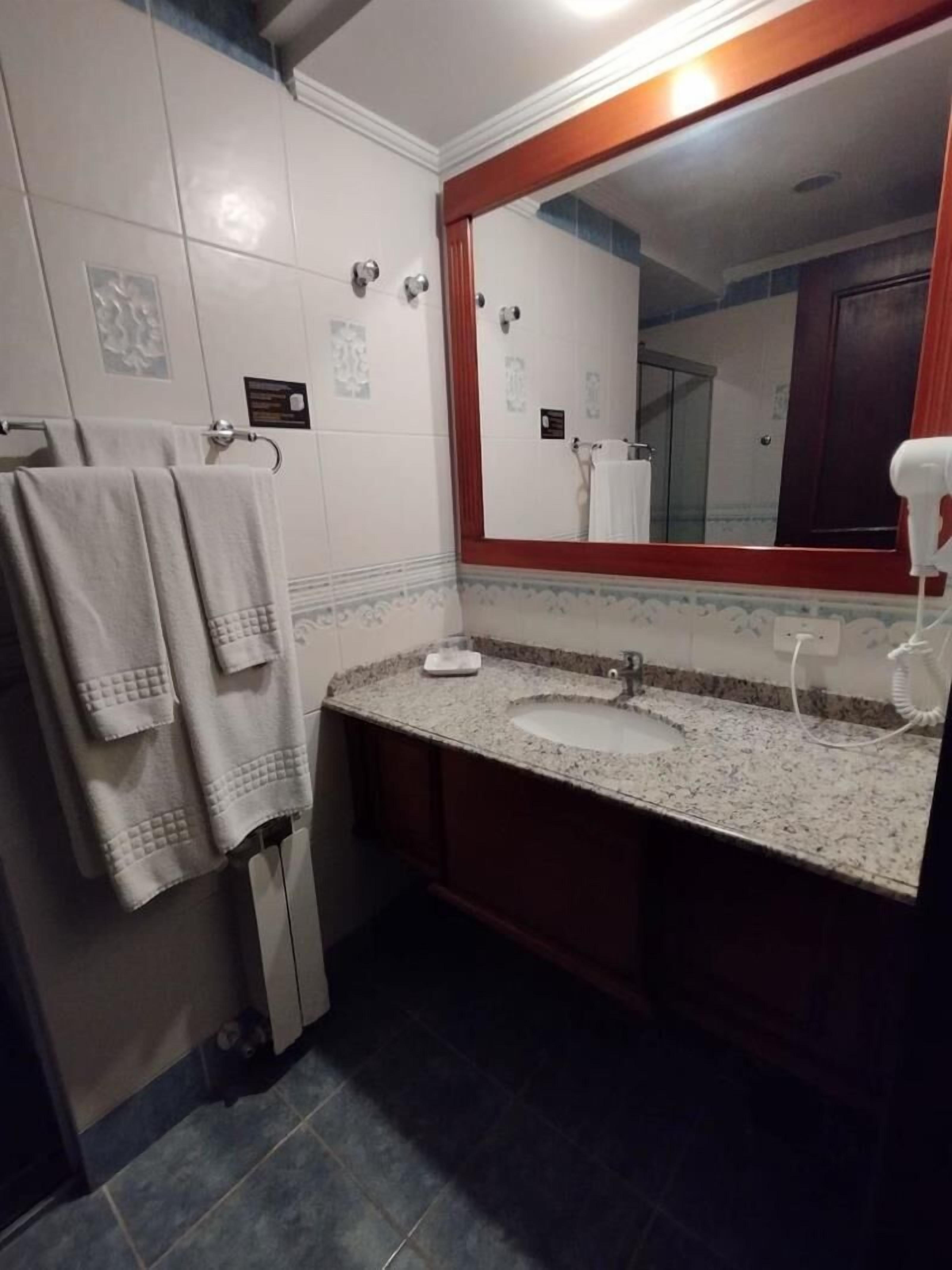 Un baño con lavamanos de encimera de granito, espejo con marco de madera y toallero con toallas dobladas.