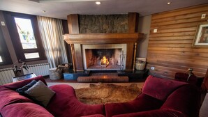 A cozy living room with a fireplace, a red velvet sofa, and a stone wall. - Hotel Serra Nevada (Canela)