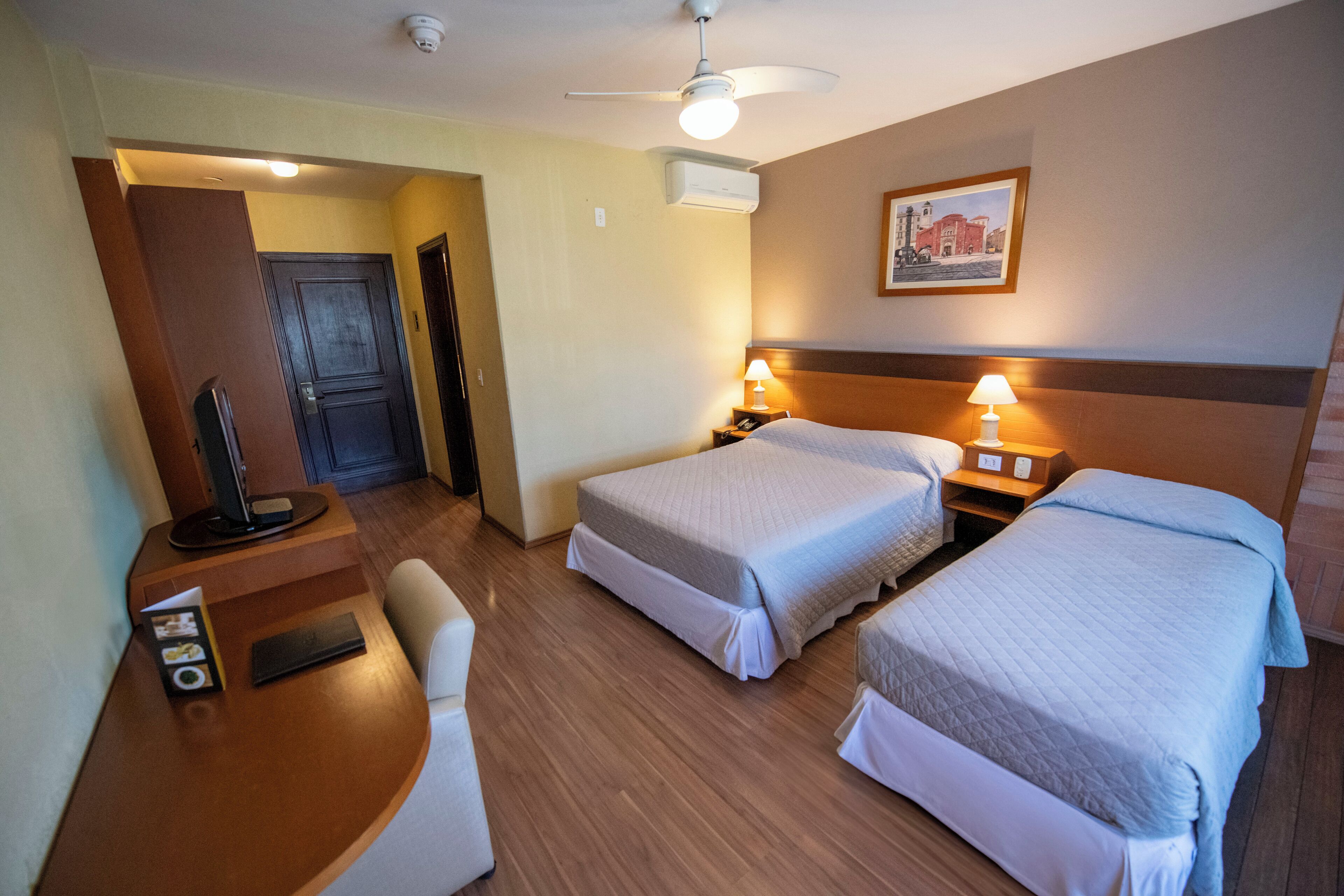A hotel room with two beds, a desk with a computer, a chair, and a ceiling fan.