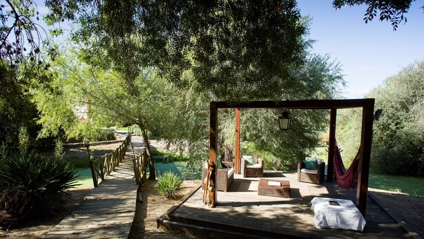 A wooden deck leading to a covered seating area with wicker furniture and a hammock.