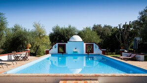 A rectangular swimming pool with a white dome structure in the center, surrounded by lounge chairs and a tiled patio area.