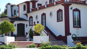 A two-story building with a white facade, red trim, and a set of stairs leading to the entrance.