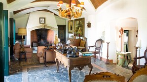 A spacious living room with a fireplace, a chandelier, and antique furniture.