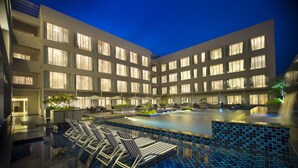 A hotel with a swimming pool, lounge chairs, and a modern building facade with multiple windows.