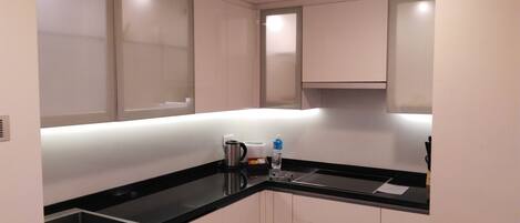 Una kitchenette compacta con mostrador negro, un hervidor, una botella de agua y una caja pequeña.