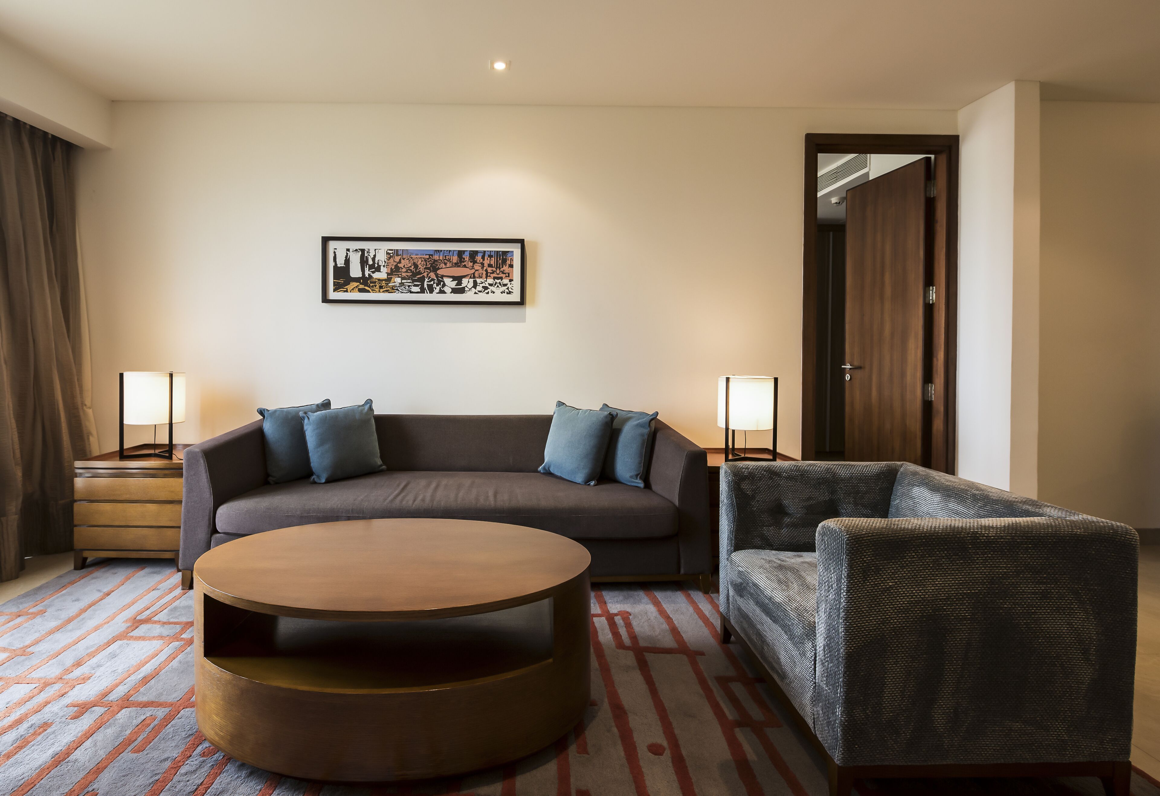 A modern hotel room with a sofa, a round coffee table, and two lamps.