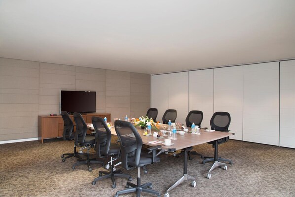 A conference room with a long table, six chairs, a TV on a stand, and a wooden desk.