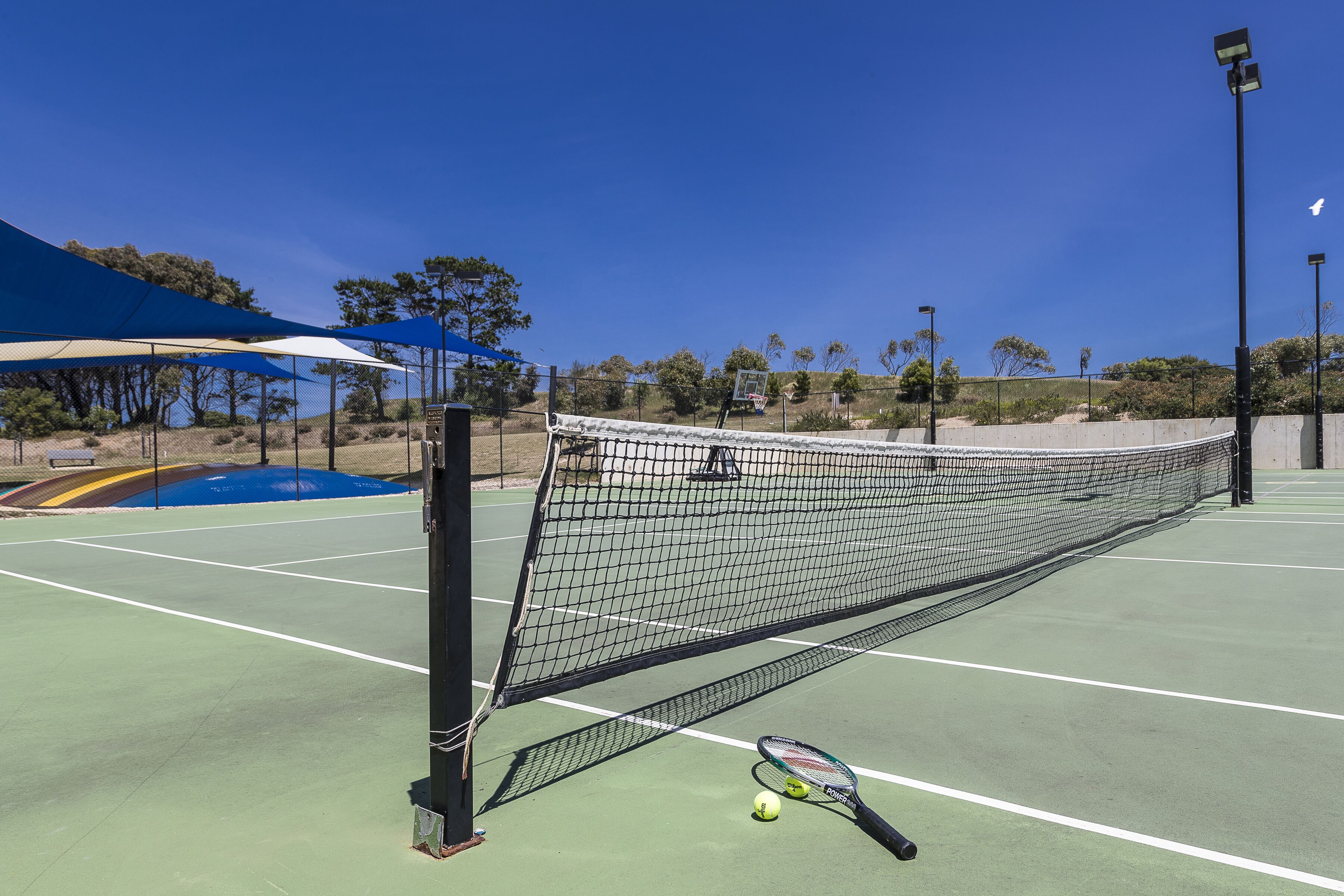 A tennis court with a net, a tennis racket, and two tennis balls.