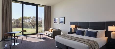A modern hotel room with a large bed, a sofa, a small table, and a view of the outdoors.