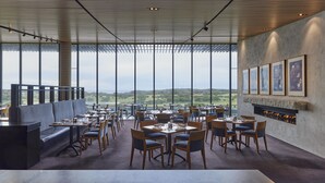 Ein modernes Restaurant mit Panoramablick, das sich durch eine hohe Decke, große Fenster und einen Kamin auszeichnet.