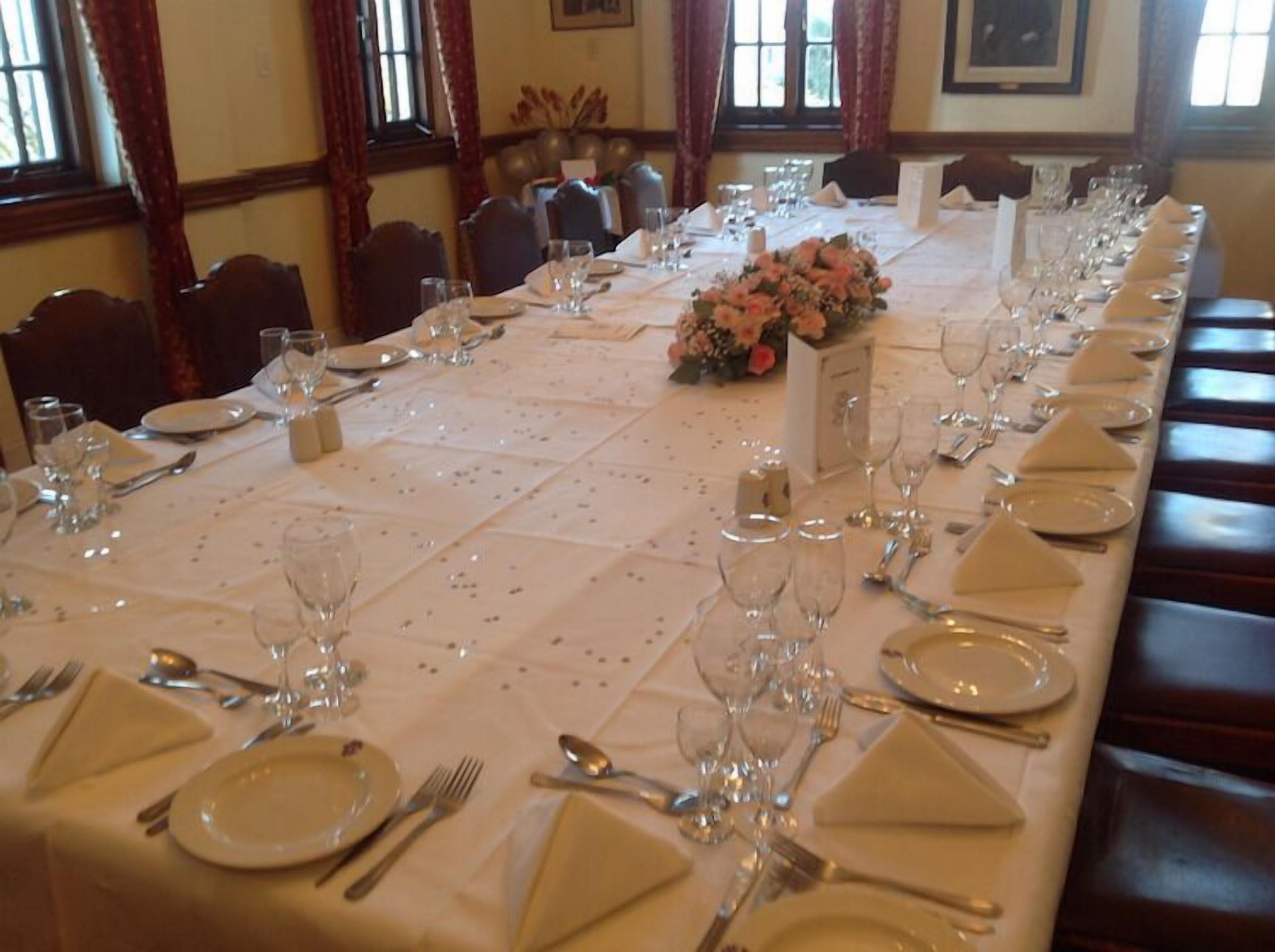 Een lange eettafel is gedekt met meerdere zitplaatsen, inclusief borden, bestek en glazen.