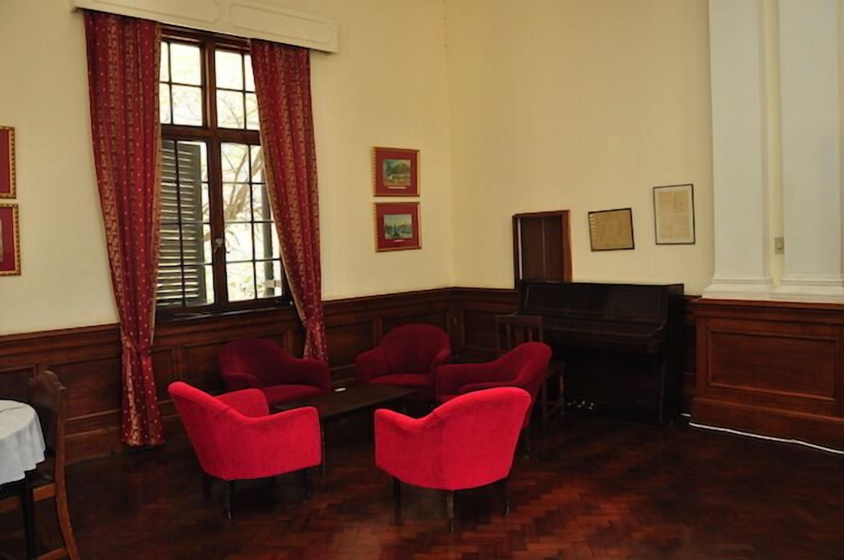 A room with wooden paneling, a piano, red upholstered chairs, and framed pictures on the wall.