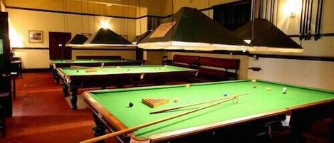 A pool hall with multiple pool tables, each with a green felt surface and a cue stick on one of them.