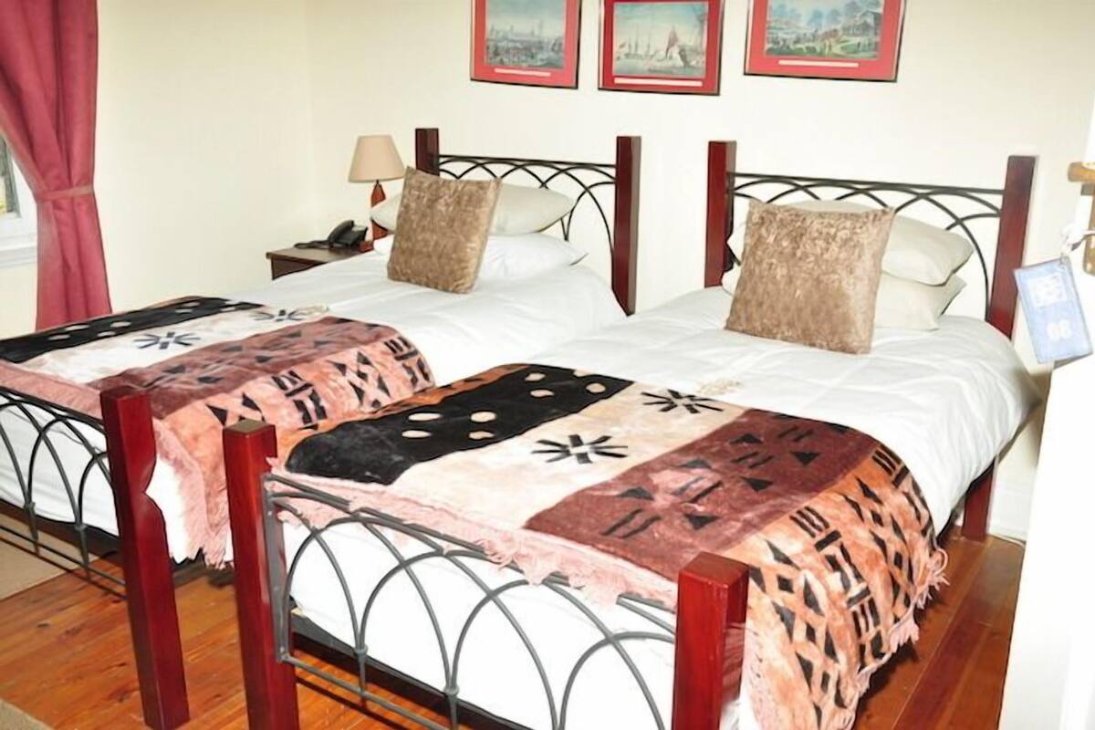 A double bed with a patterned bedspread, a nightstand with a lamp, and a framed picture on the wall.