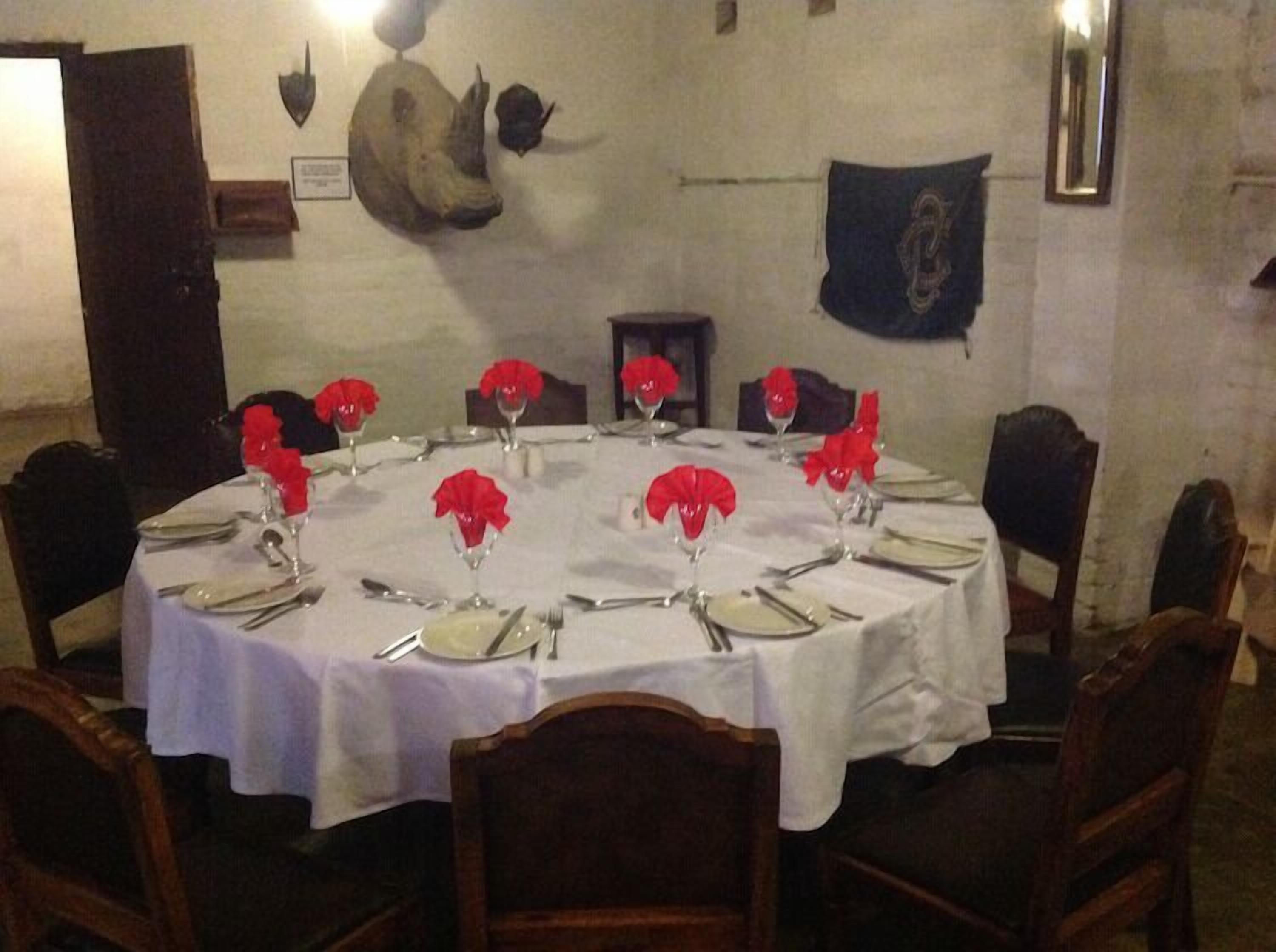 A round dining table set for six with white tablecloths, red napkins, and silverware.