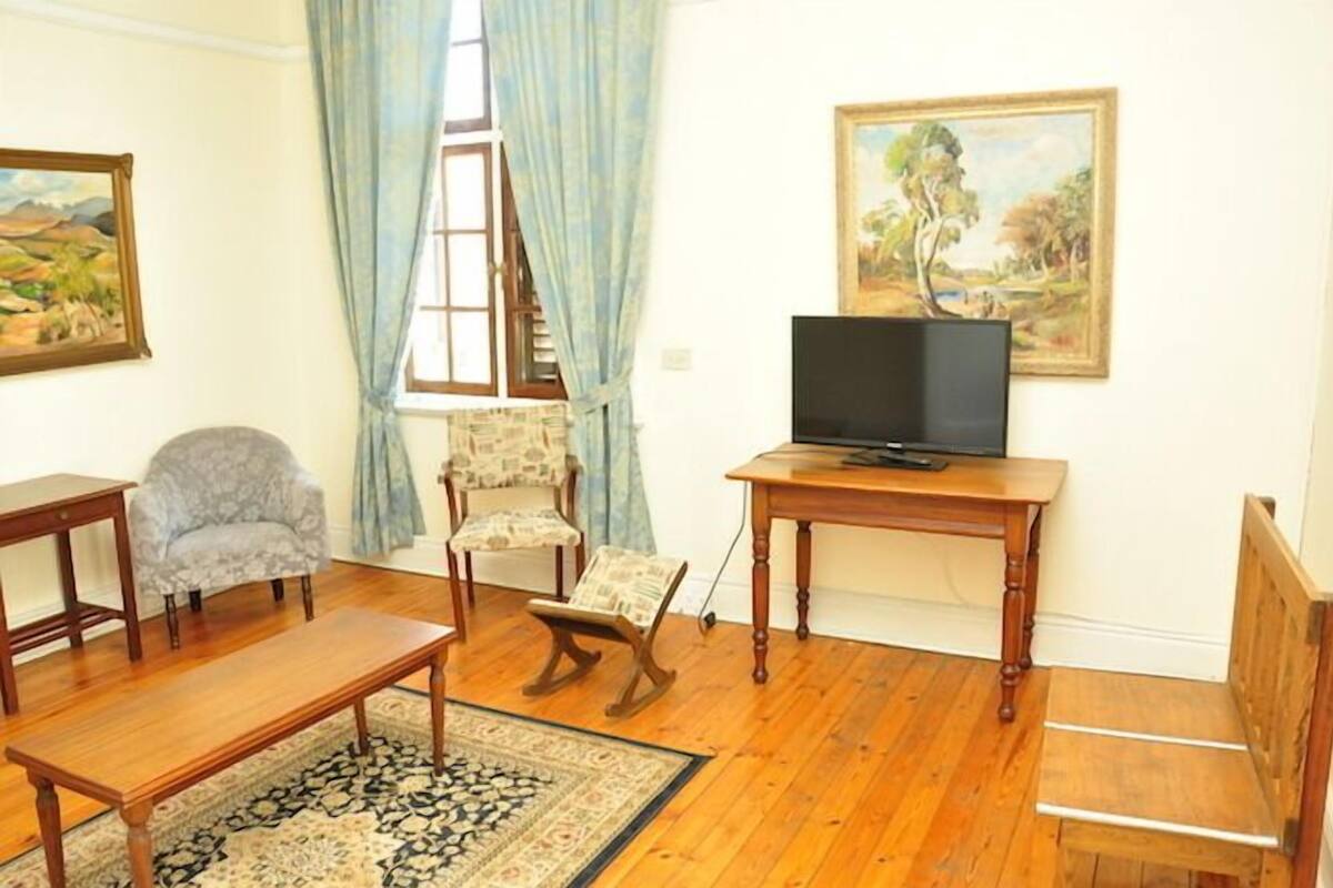 A living room with a wooden floor, a sofa, a chair, a small table with a TV, and a painting on the wall.